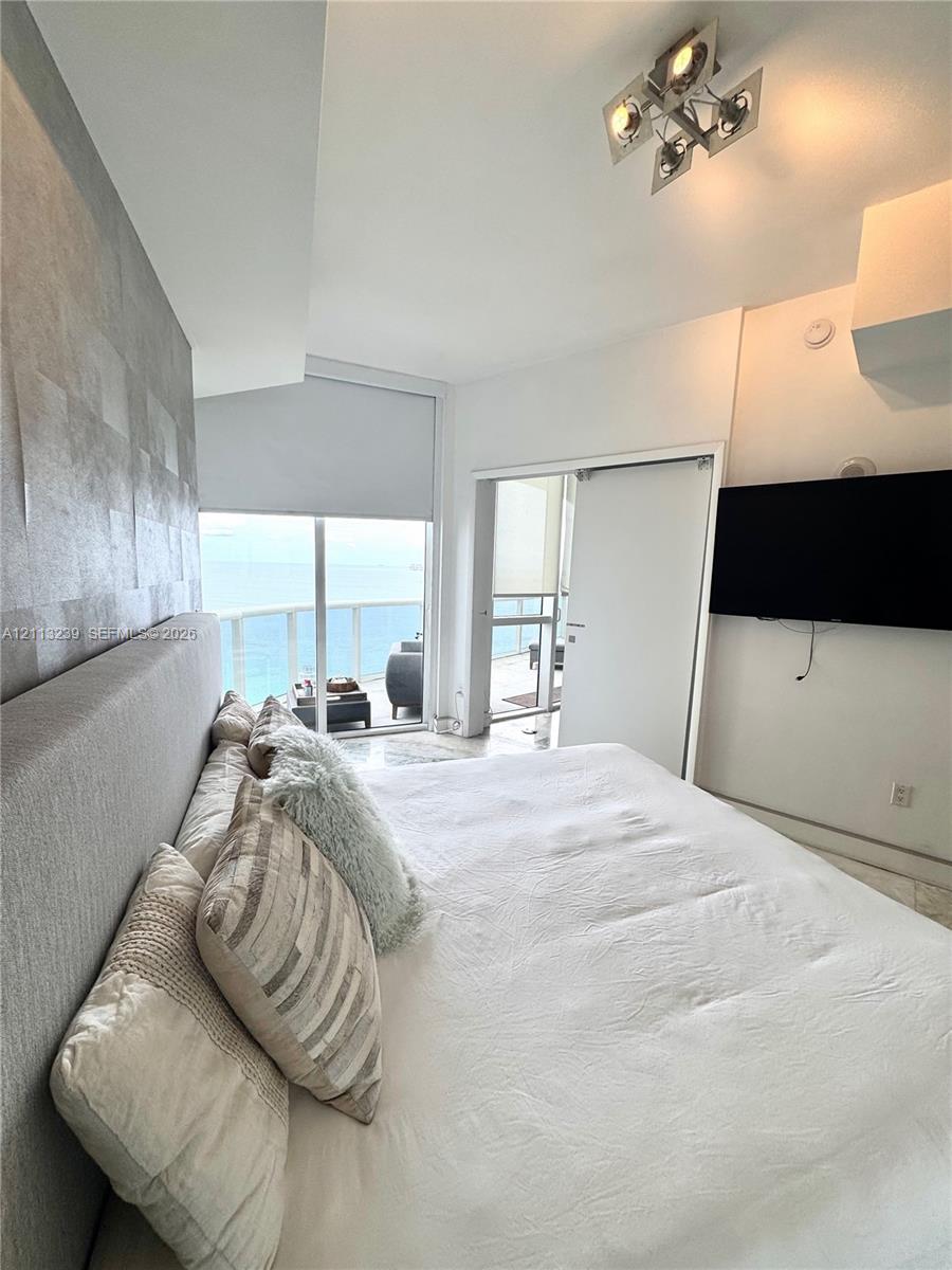 Textured feature wall with metallic finish, floor-to-ceiling glass sliding door, balcony access, and geometric ceiling-mounted light fixture