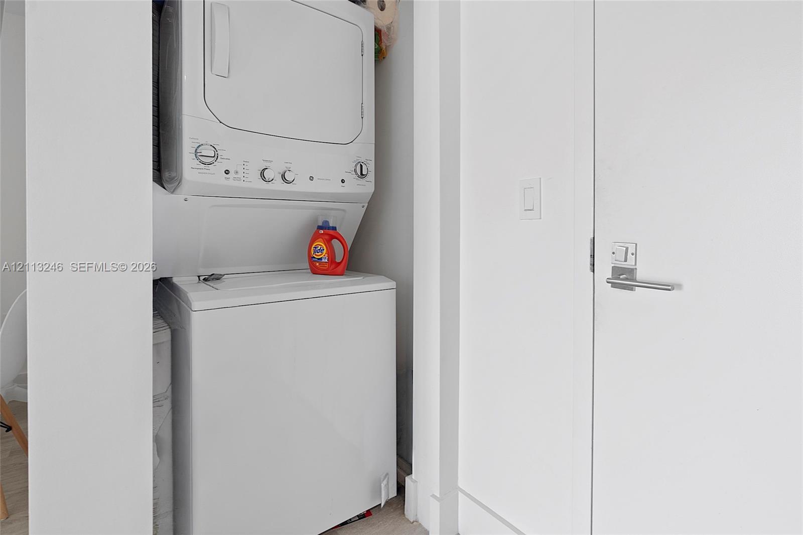 Stacked white washer and dryer unit housed within a dedicated laundry alcove featuring a swing door with a modern satin nickel lever handle