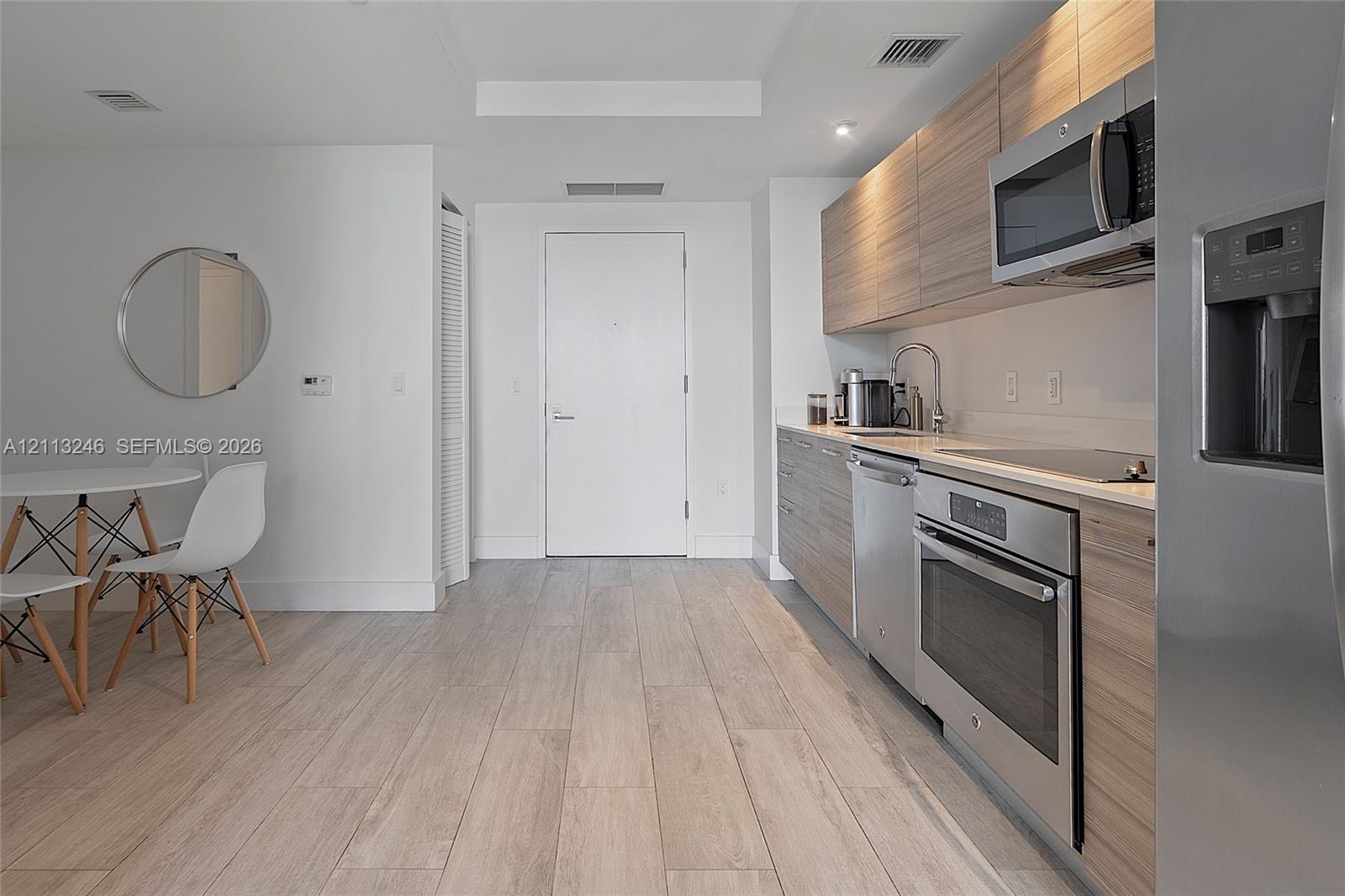 Kitchen featuring wood-finish cabinetry, stainless steel appliances, and solid-surface countertops, complemented by wood-finish flooring