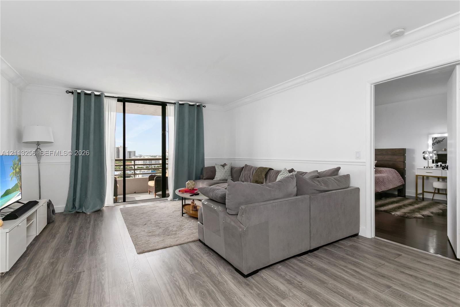 Living space featuring wood-finish flooring, crown molding, chair rail trim, and sliding glass doors opening to a balcony Living space featuring wood-finish flooring, crown molding, chair rail trim, and sliding glass doors opening to a balcony