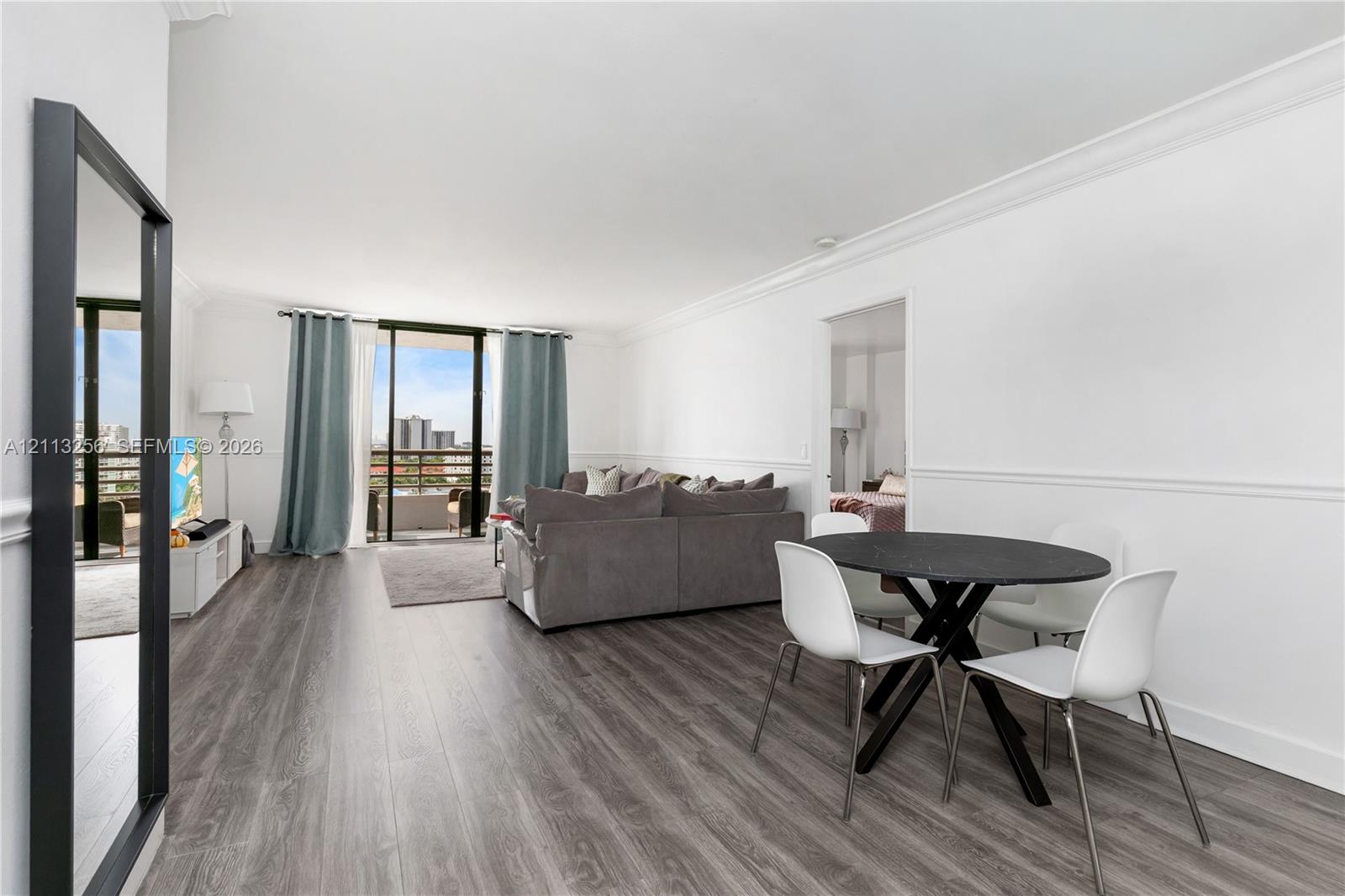 Open-concept living space featuring wood-finish flooring, crown molding, chair rail trim, and glass sliding doors providing exterior balcony access Open-concept living space featuring wood-finish flooring, crown molding, chair rail trim, and glass sliding doors providing exterior balcony access