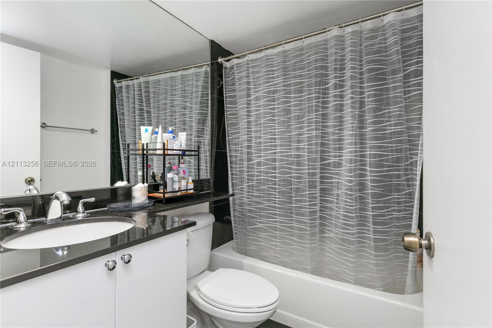 Bathroom featuring a vanity with dark stone countertop, integrated sink, polished chrome faucet, full-width mirror, and a built-in shower and tub combination.