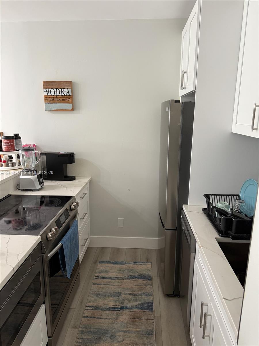 Kitchen featuring white cabinetry, quartz-style countertops, stainless steel appliances, and wood-finish flooring Kitchen featuring white cabinetry, quartz-style countertops, stainless steel appliances, and wood-finish flooring