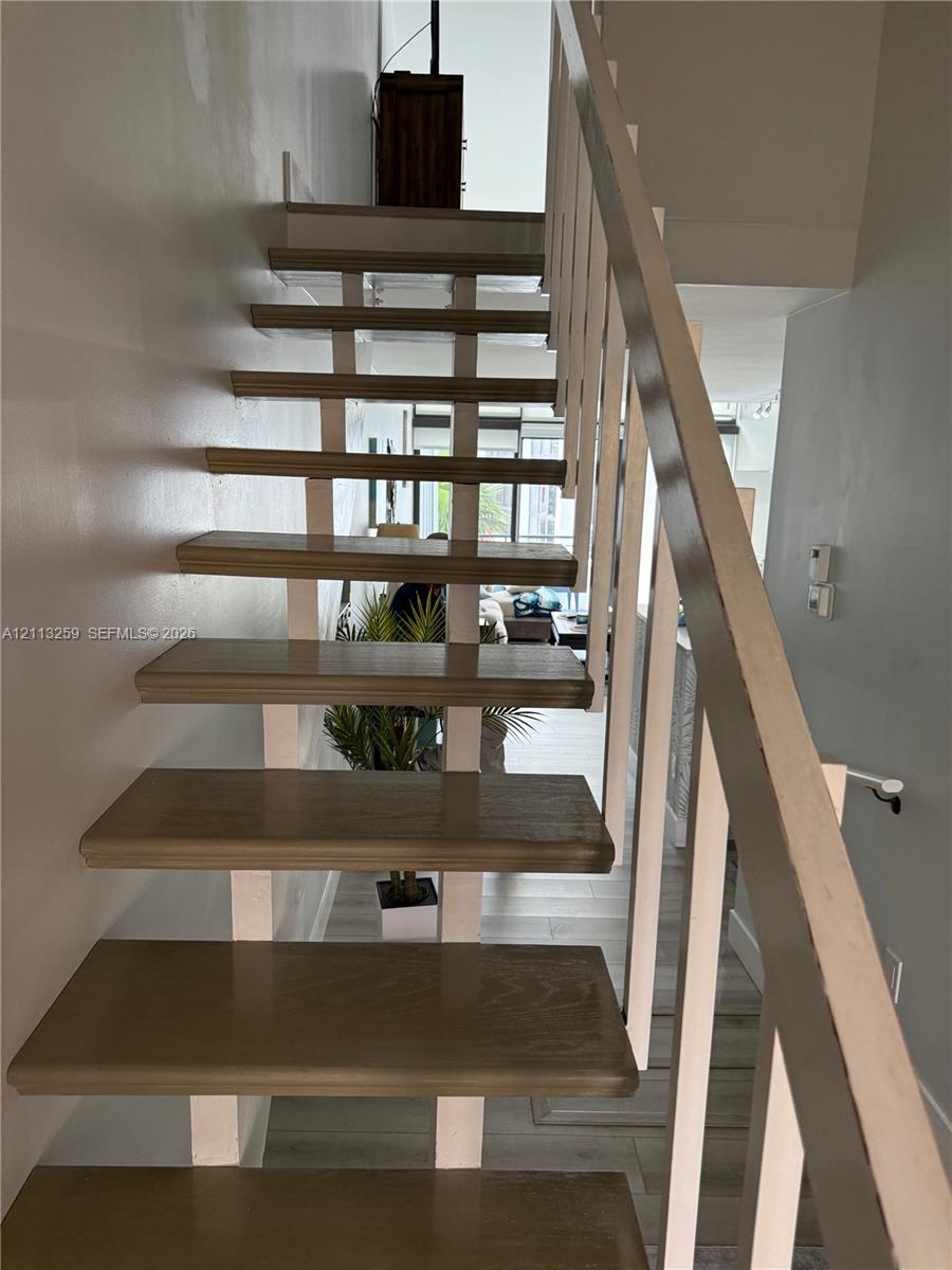 Open-riser staircase featuring wood-finish treads and a minimalist white metal railing