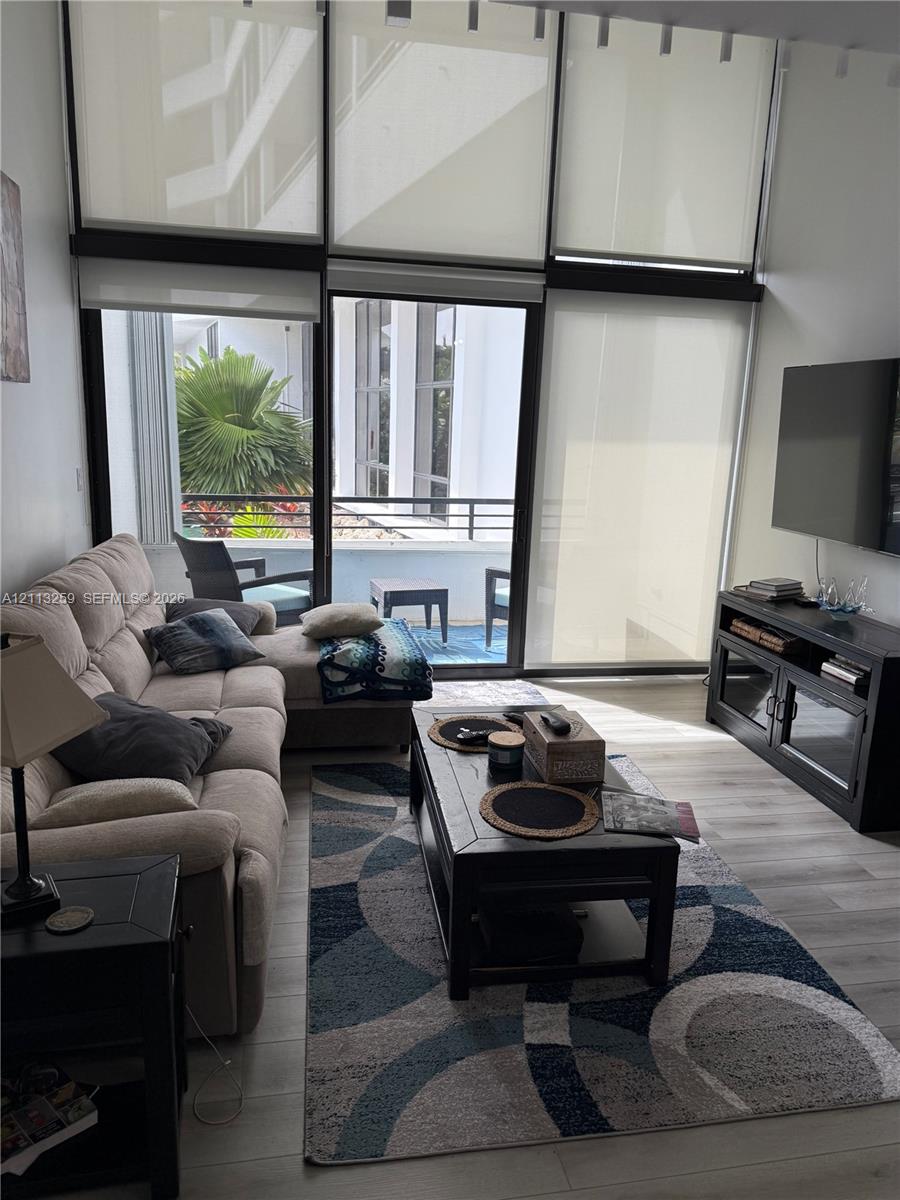 Floor-to-ceiling windows with roller shades, wood-finish flooring, and sliding glass door opening to a private balcony Floor-to-ceiling windows with roller shades, wood-finish flooring, and sliding glass door opening to a private balcony