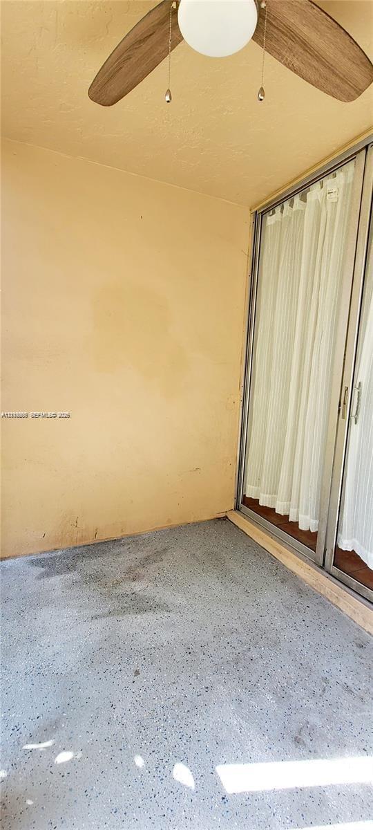 Covered exterior patio featuring a concrete floor, ceiling-mounted fan with light fixture, and sliding glass door