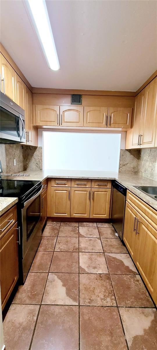 Kitchen featuring wood cabinetry, stone-finish countertops, tile flooring, stainless steel appliances, and integrated linear lighting