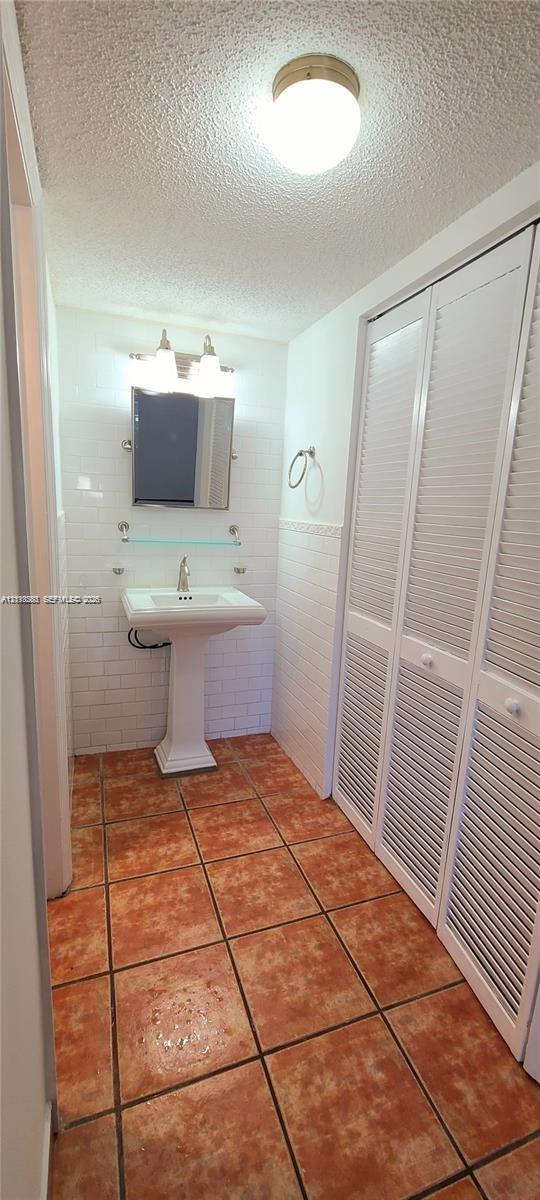 White pedestal sink with a chrome faucet, ceramic subway tile backsplash, glass shelf, louvered-panel closet doors, and earth-tone ceramic tile flooring