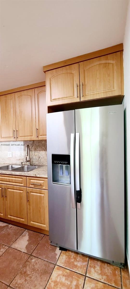 Kitchen area featuring light-finish cabinetry, stone-surface countertops, stainless steel side-by-side refrigerator, dual-basin stainless steel sink with high-arc faucet, and tiled flooring