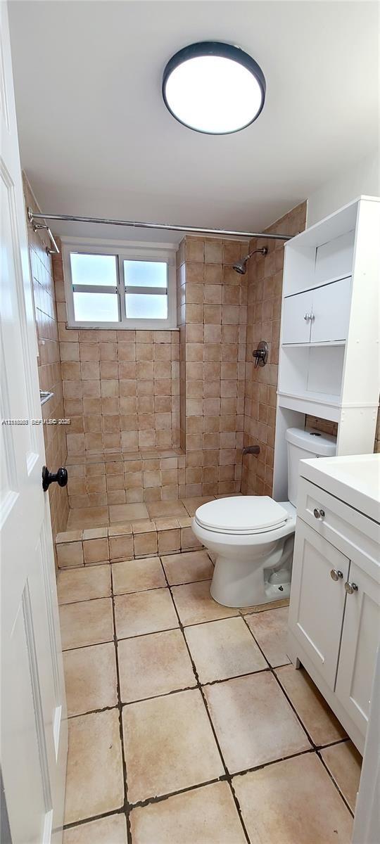Bathroom featuring tile flooring, a walk-in shower with tiled surround, a white vanity cabinet, a wall-mounted medicine cabinet, and a flush-mount ceiling light