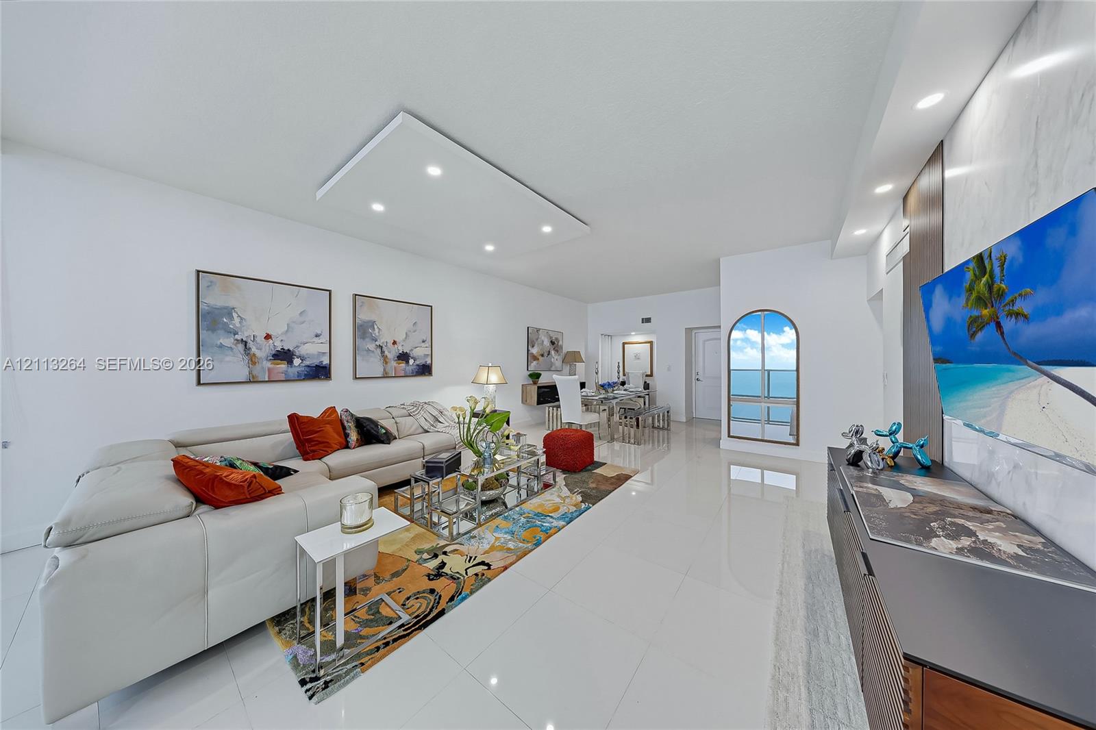Open-concept living space featuring high-gloss tile flooring, recessed ceiling lighting, a custom stone-clad media wall, and an arched glass door Open-concept living space featuring high-gloss tile flooring, recessed ceiling lighting, a custom stone-clad media wall, and an arched glass door