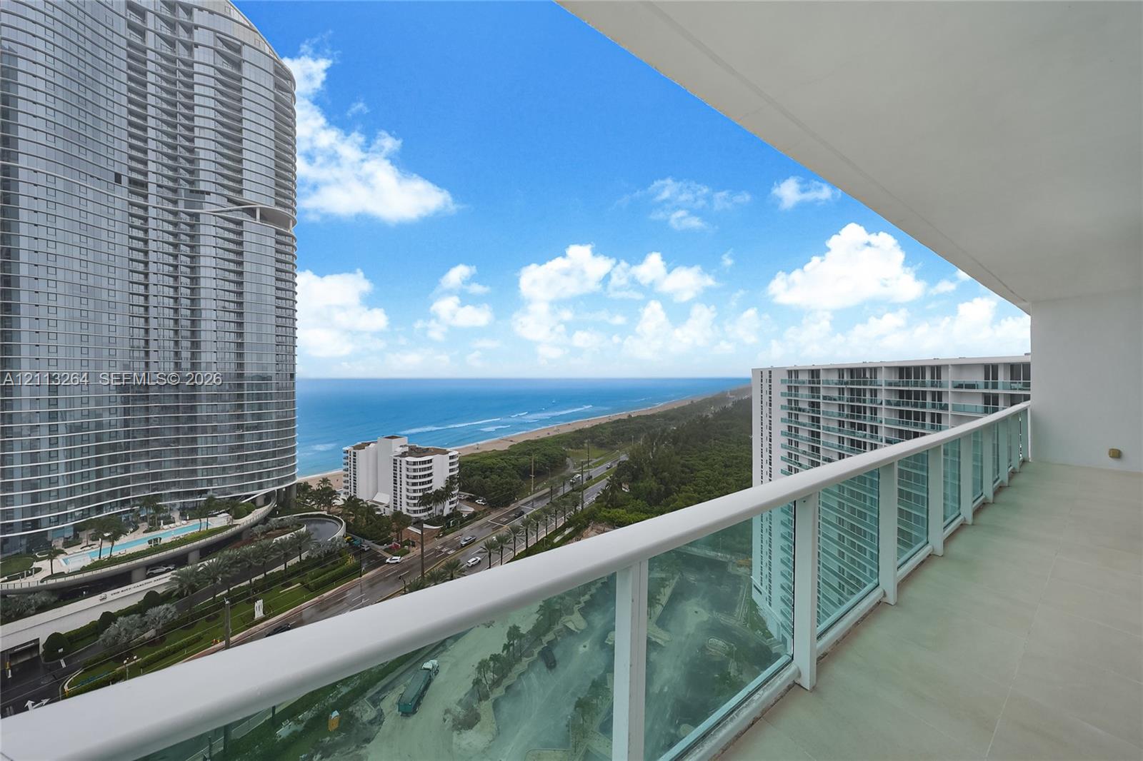 Covered balcony featuring tile flooring and a glass-paneled railing overlooking the coastline and ocean Covered balcony featuring tile flooring and a glass-paneled railing overlooking the coastline and ocean