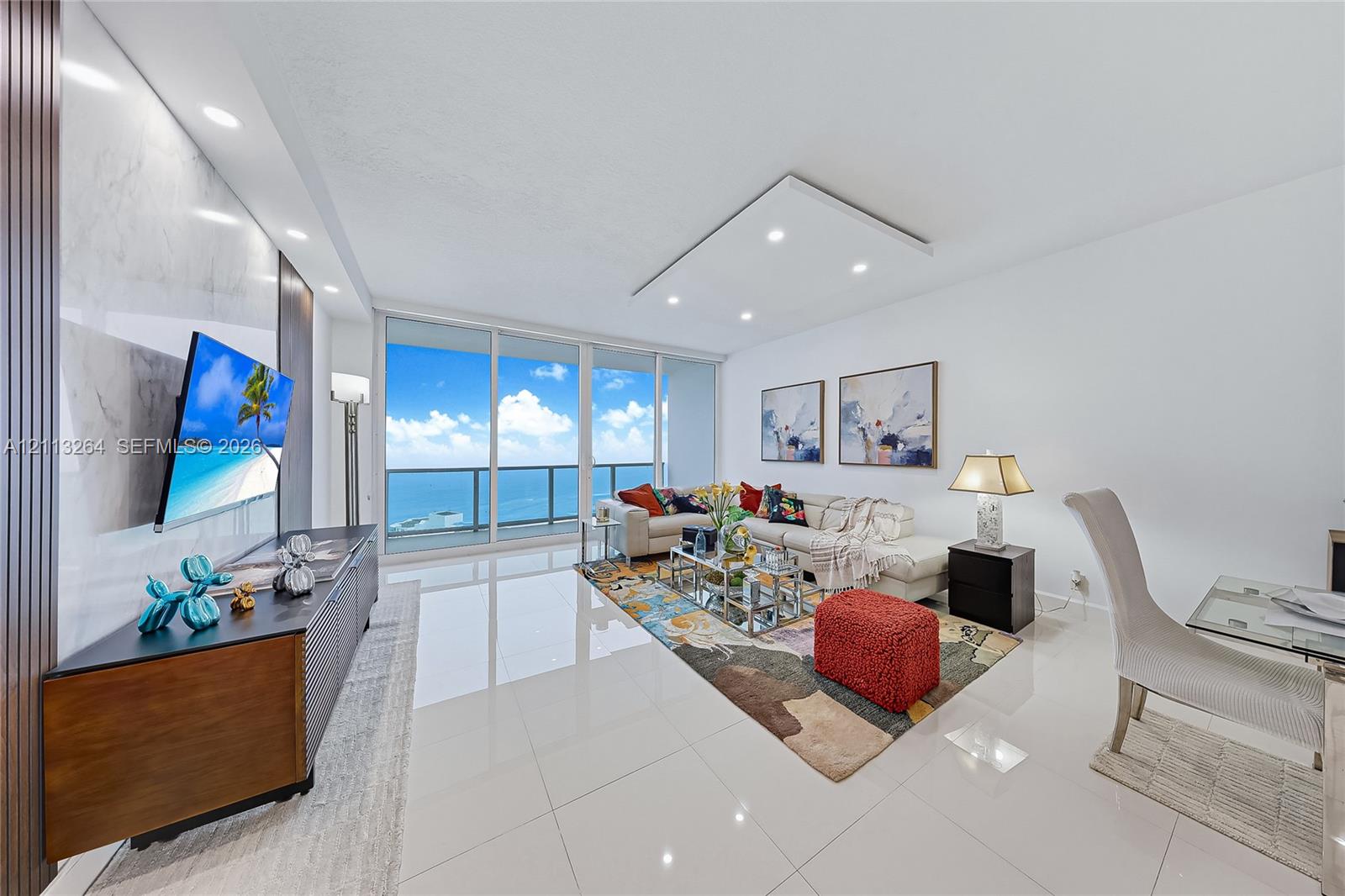 Living area featuring floor-to-ceiling glass sliding doors, polished tile flooring, recessed ceiling lighting, and a floor-to-ceiling stone-finish accent wall Living area featuring floor-to-ceiling glass sliding doors, polished tile flooring, recessed ceiling lighting, and a floor-to-ceiling stone-finish accent wall