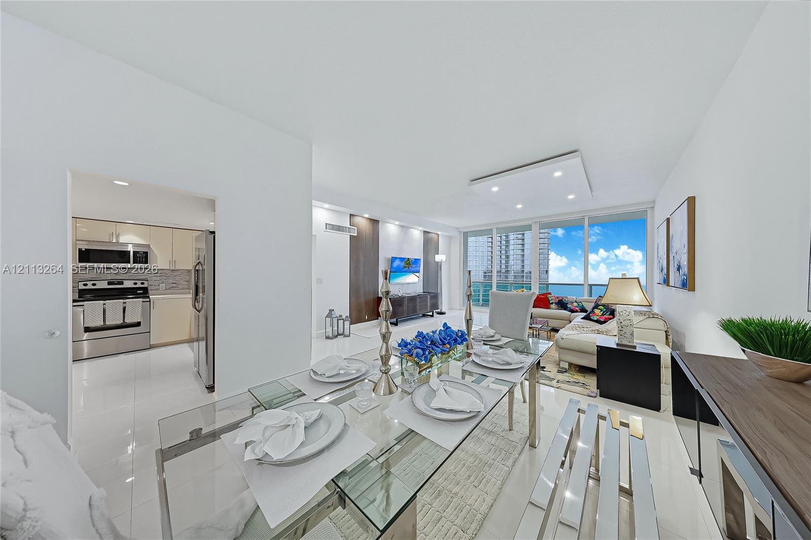 Open-concept interior featuring large-format tile flooring, recessed ceiling lighting, full-height windows, and integrated kitchen appliances Open-concept interior featuring large-format tile flooring, recessed ceiling lighting, full-height windows, and integrated kitchen appliances