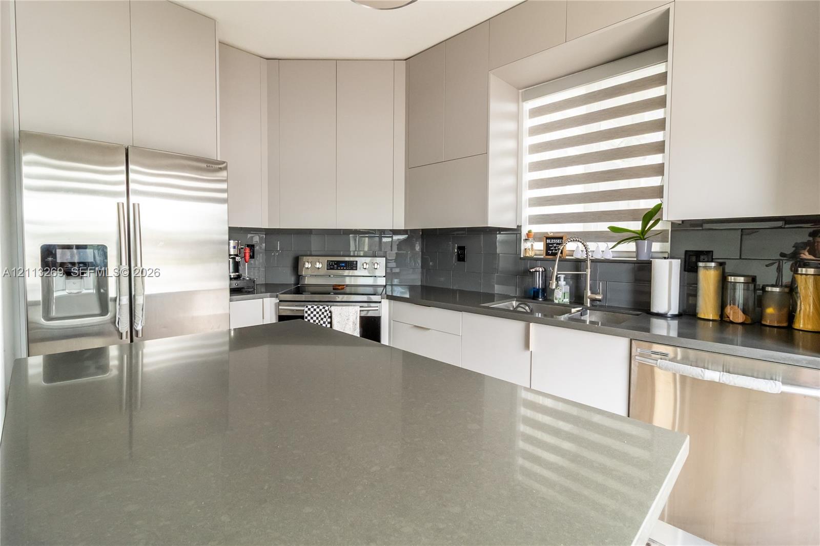 Contemporary kitchen featuring flat-panel cabinetry, solid-surface countertops, a full-height tile backsplash, and stainless-steel appliances