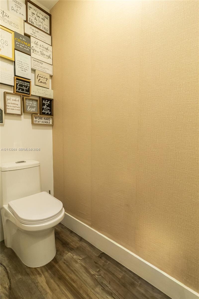 Powder room featuring a two-piece toilet, textured wall covering, and wood-finish flooring