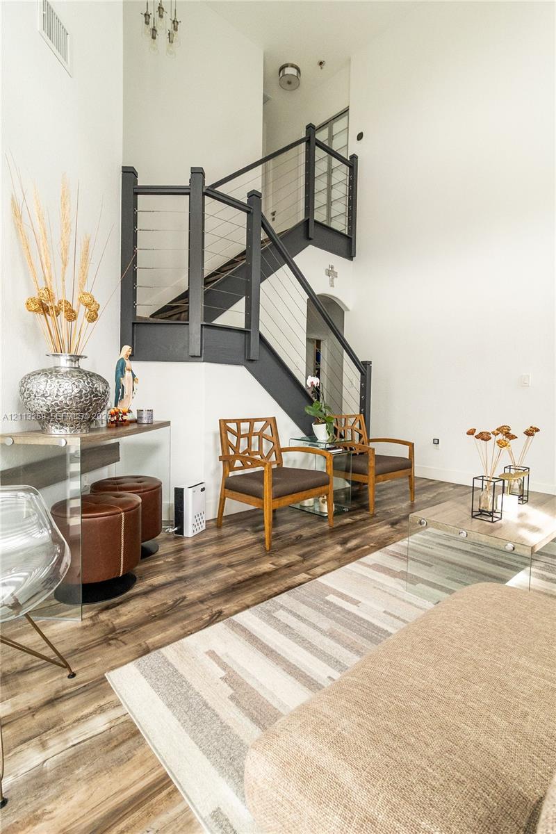 Staircase featuring dark-finished wooden railings and integrated stainless steel cable balusters, complemented by high-vaulted ceilings and wood-finish flooring