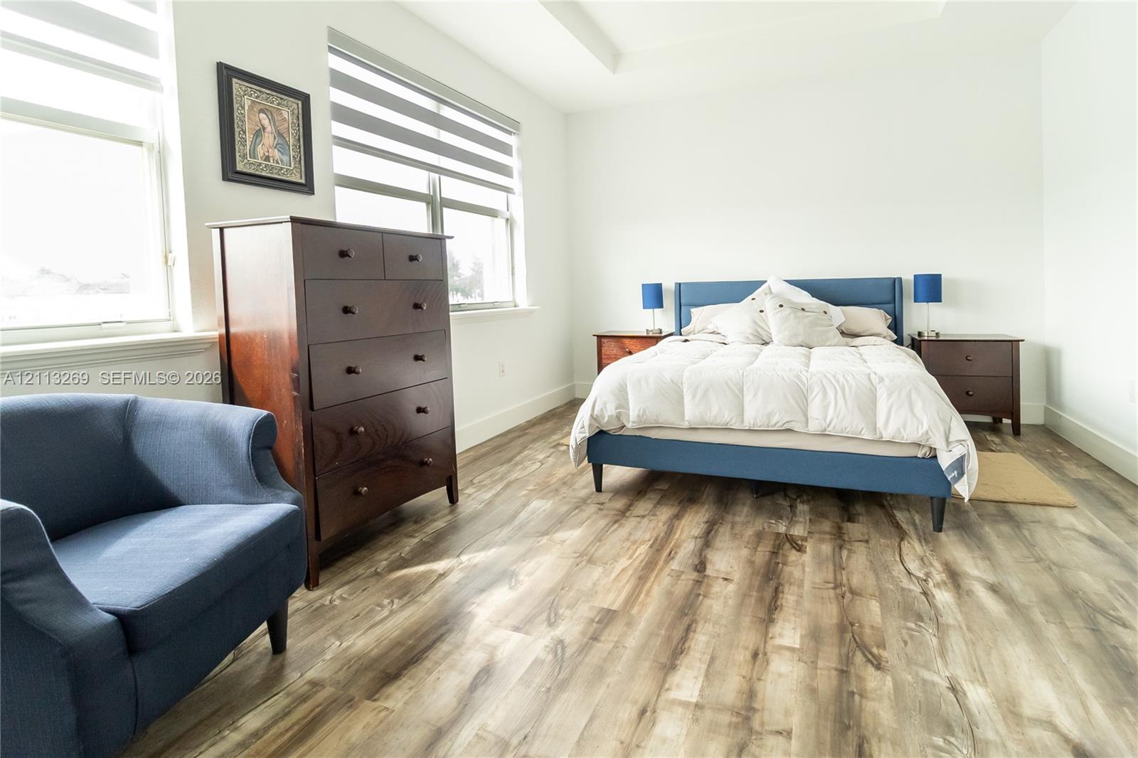 Bedroom featuring high ceilings, wood-finish flooring, and large windows with dual-layer adjustable blinds