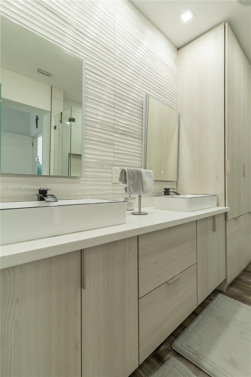 Double vanity featuring wood-finish cabinetry, rectangular vessel sinks, matte black faucets, quartz-style countertops, and textured wall tile