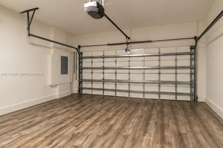 Enclosed garage featuring wood-finish flooring, a metal sectional door, and an overhead automatic opener