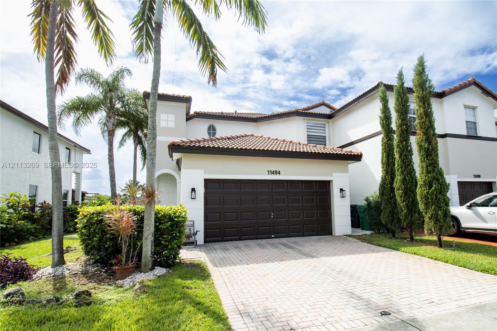 Stucco exterior featuring a clay tile roof, paved driveway, attached garage, and landscaping