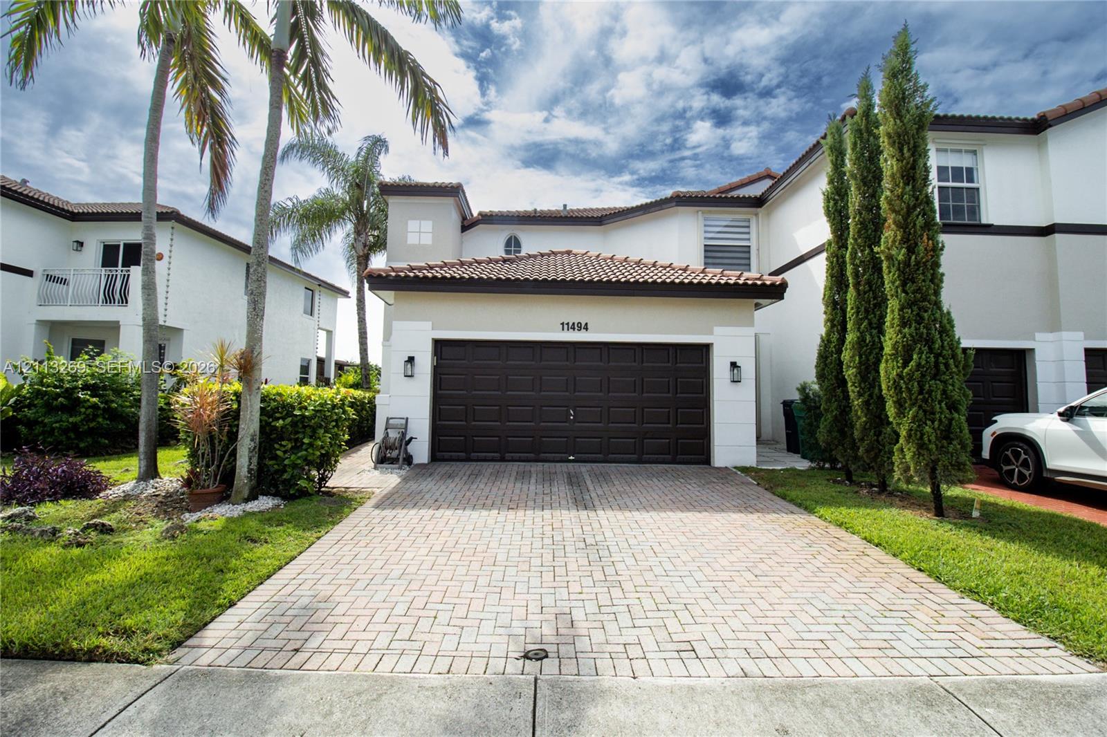 Stucco exterior featuring a tile roof, paved driveway, dark-toned sectional garage door, and exterior wall-mounted lighting