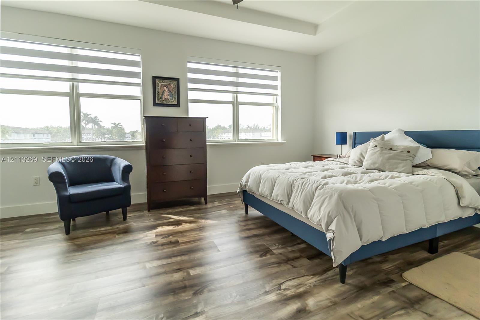 Room featuring wood-finish flooring, tray ceiling, and dual large windows with horizontal blinds
