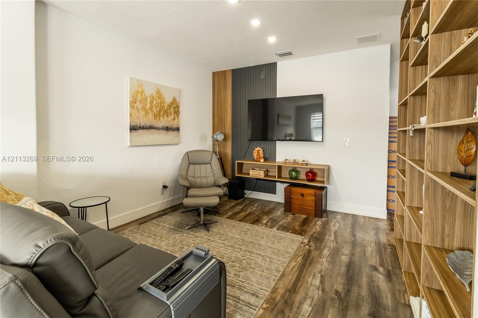 Custom floor-to-ceiling wood-finish shelving unit, wood-finish flooring, and a dedicated wall feature accented with vertical charcoal paneling and a floating media shelf