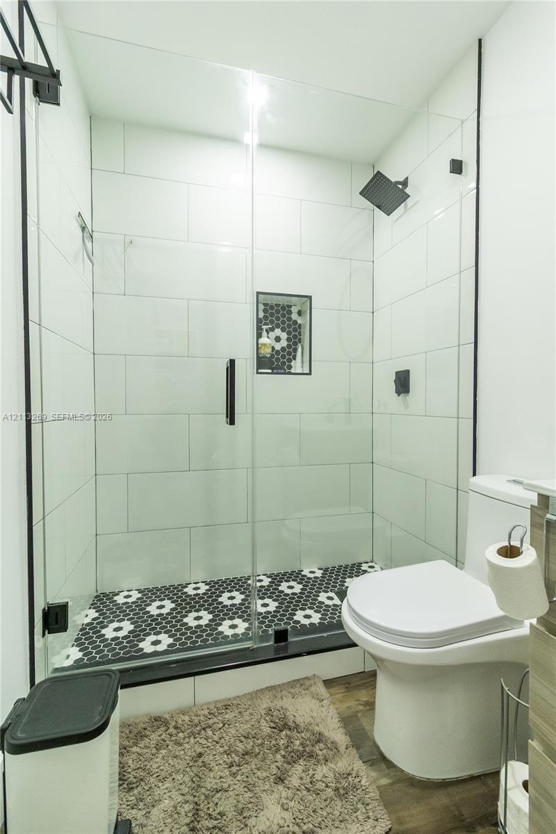 Walk-in shower with floor-to-ceiling white subway tile, black-and-white patterned tile flooring, built-in shower niche, glass enclosure, and matte black hardware