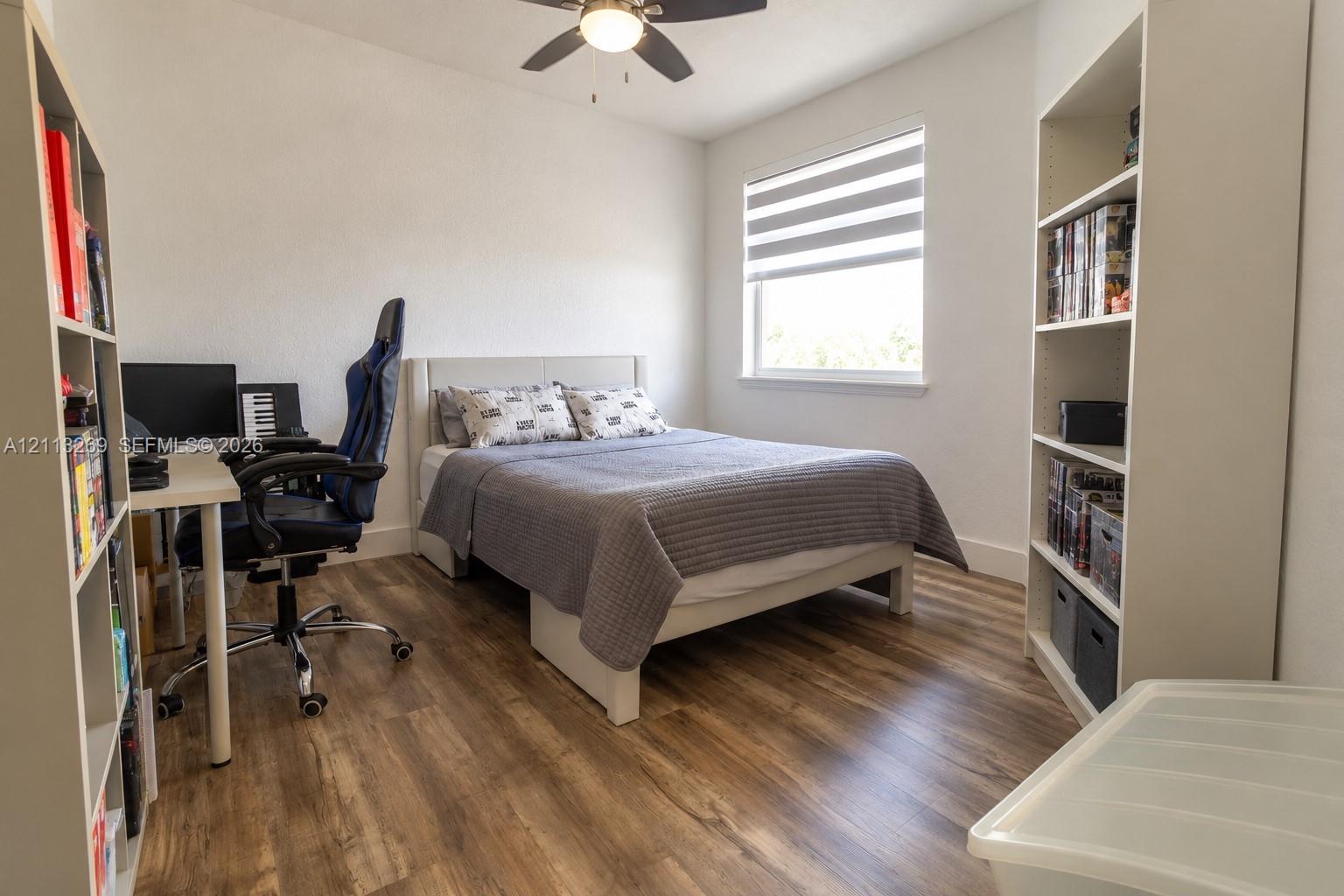 Room featuring wood-finish flooring, a ceiling fan with integrated lighting, and a window with dual-layer shade