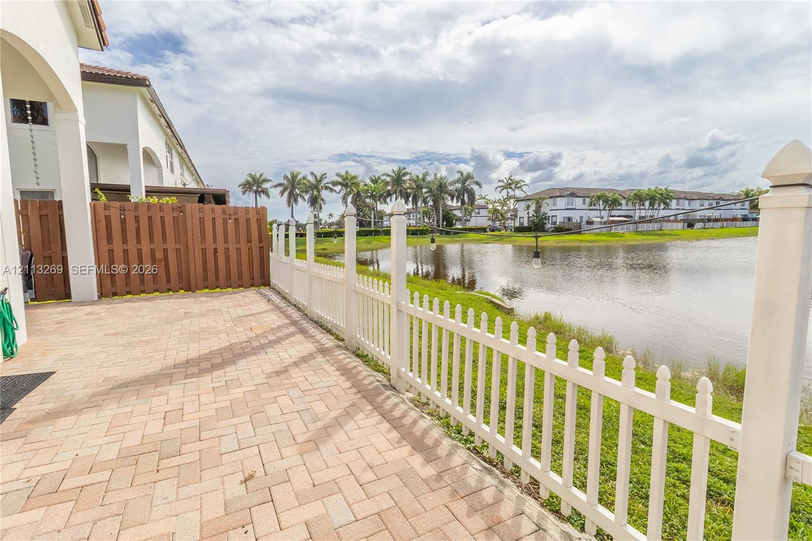 Paver patio featuring a privacy fence and white picket fencing overlooking a water feature