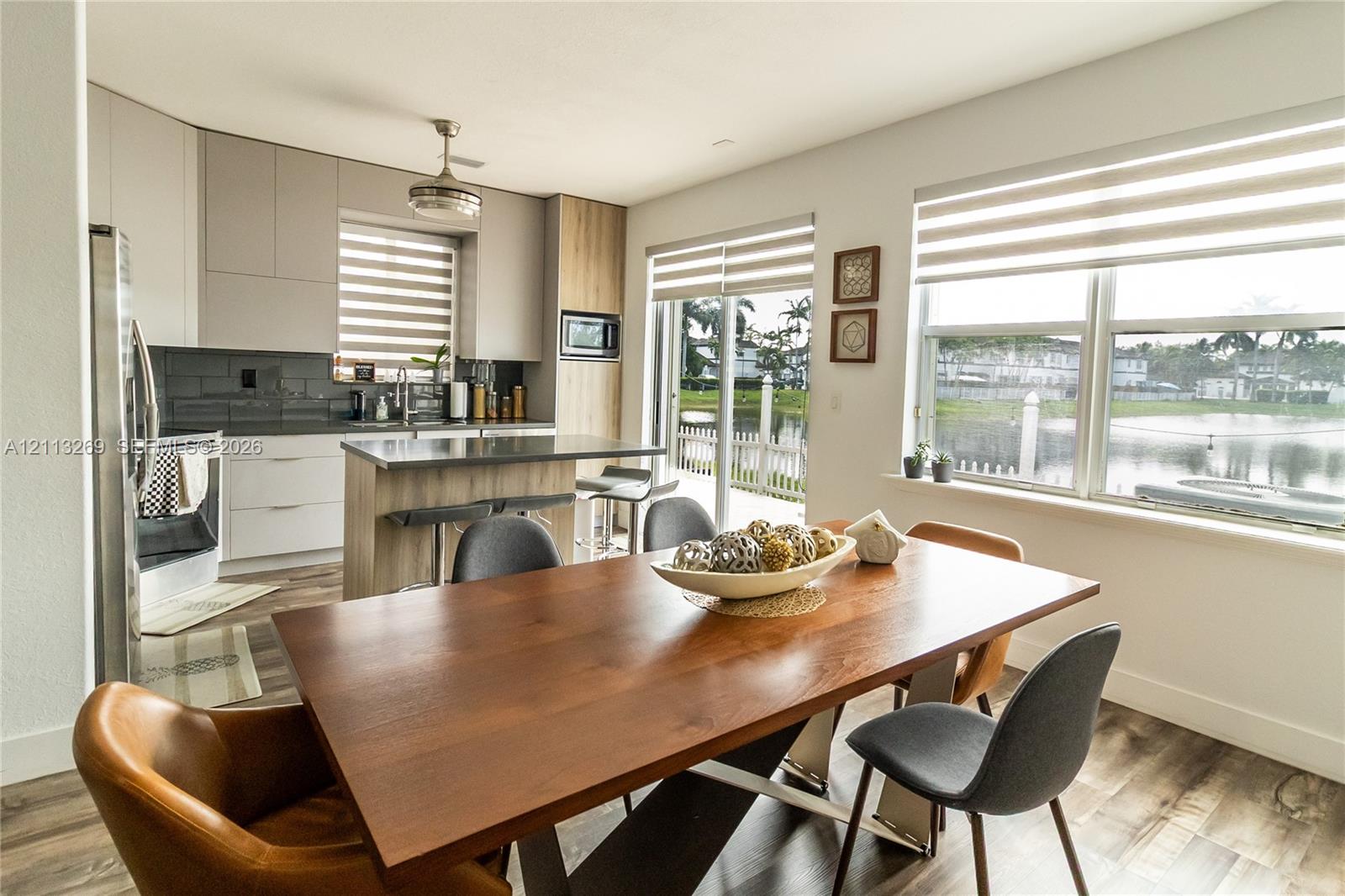 Kitchen featuring flat-panel cabinetry, a central island, wood-finish flooring, tiled backsplash, and large windows with integrated blinds