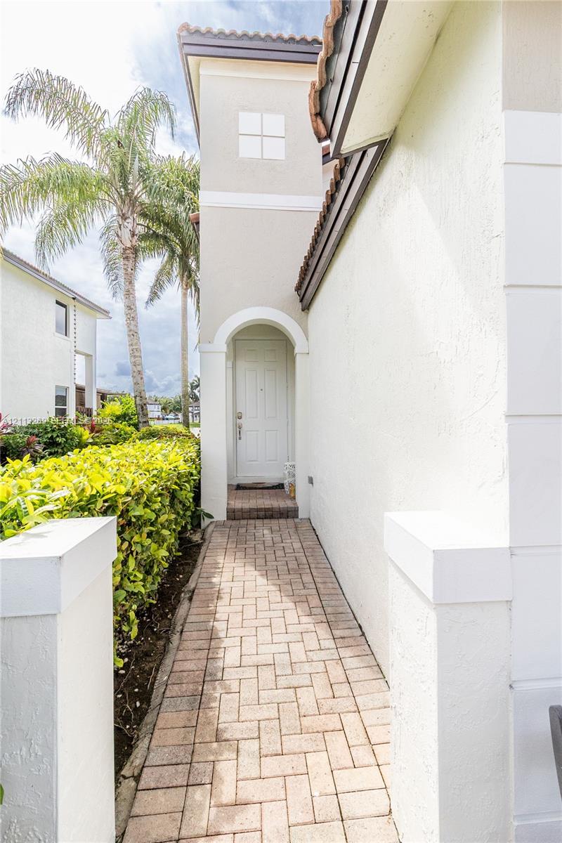 Exterior entryway featuring a paver stone walkway, arched recessed doorway, and stucco facade with a tile roof accent