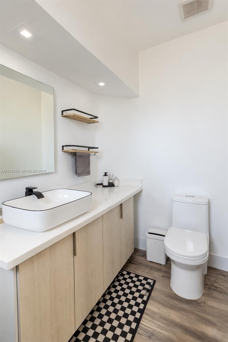 Light-toned cabinetry with a white countertop, vessel sink, matte black faucet, wall-mounted shelving, and wood-finish flooring