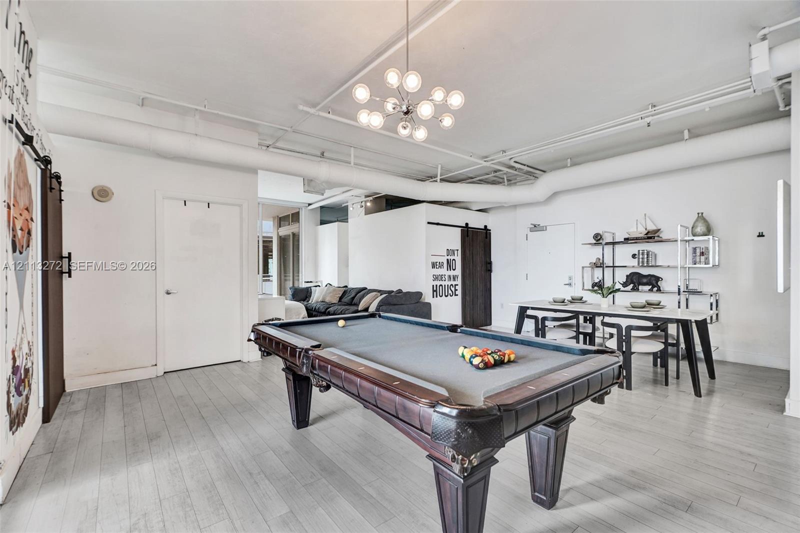 Open-concept industrial-style interior featuring high ceilings with exposed ductwork, wood-finish flooring, modern multi-globe chandelier, and a dark wood barn door with black hardware