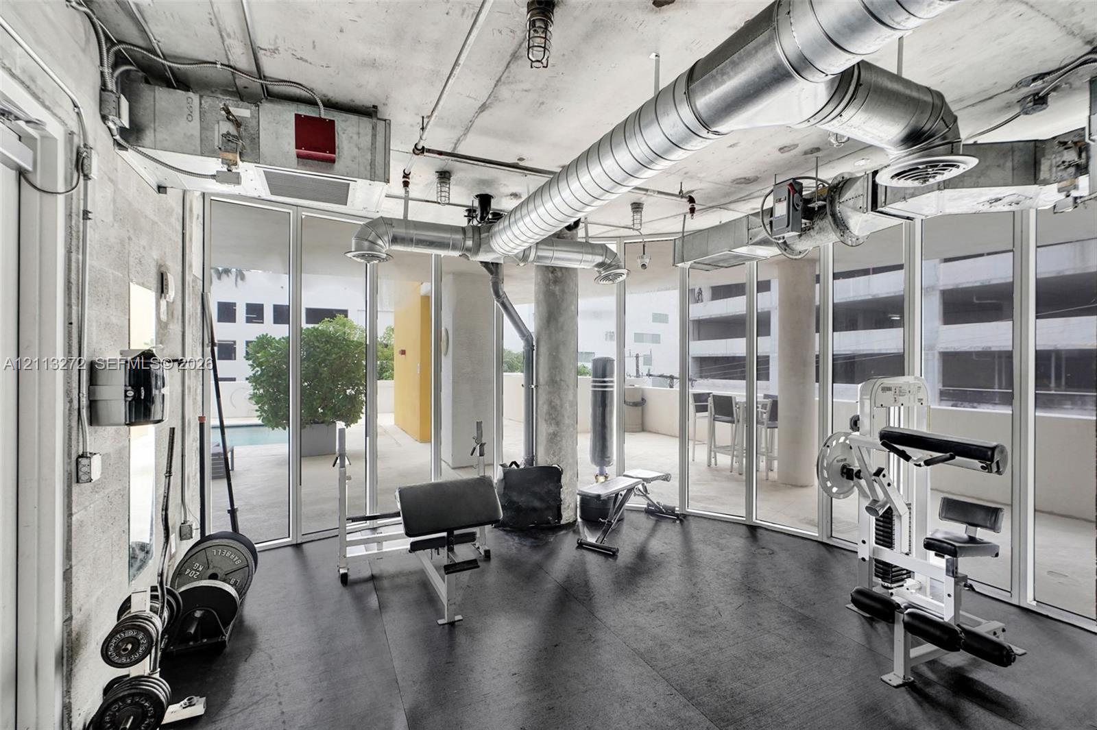 Industrial-style interior featuring exposed concrete ceilings, metallic ductwork, floor-to-ceiling glass wall panels, and impact-resistant rubber flooring