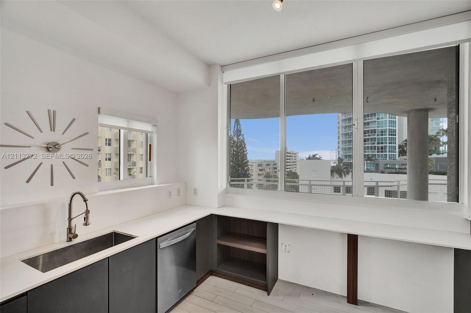 Kitchen featuring expansive window walls, stainless steel undermount sink with gooseneck faucet, integrated dishwasher, dark cabinetry with flat-panel doors, and white countertops