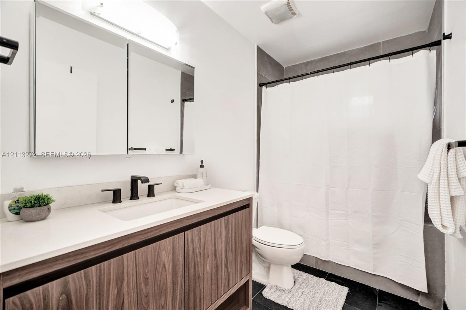 Bathroom featuring a wood-finish floating vanity, integrated rectangular sink, matte black widespread faucet, and expansive mirrored medicine cabinet