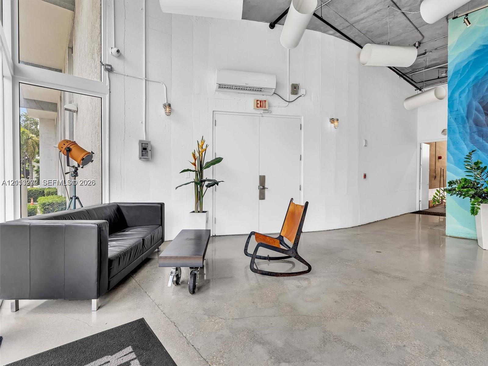 Industrial-style interior featuring polished concrete flooring, exposed ceiling with cylindrical ductwork, floor-to-ceiling windows, and a curved architectural wall