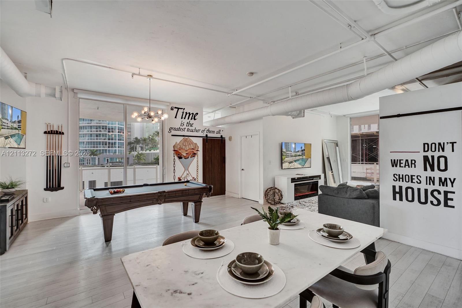 Open-concept living space featuring high ceilings with exposed ductwork, wood-finish flooring, floor-to-ceiling glass sliding doors, and a rustic sliding barn door