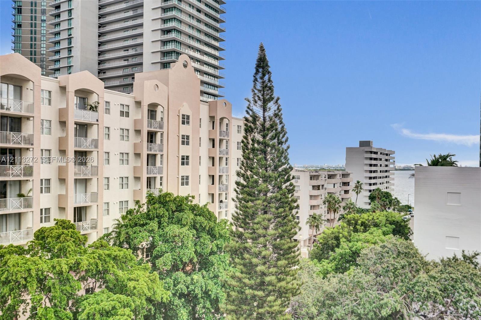 Exterior elevation featuring arched architectural details, integrated private balconies with metal railings, and lush mature trees