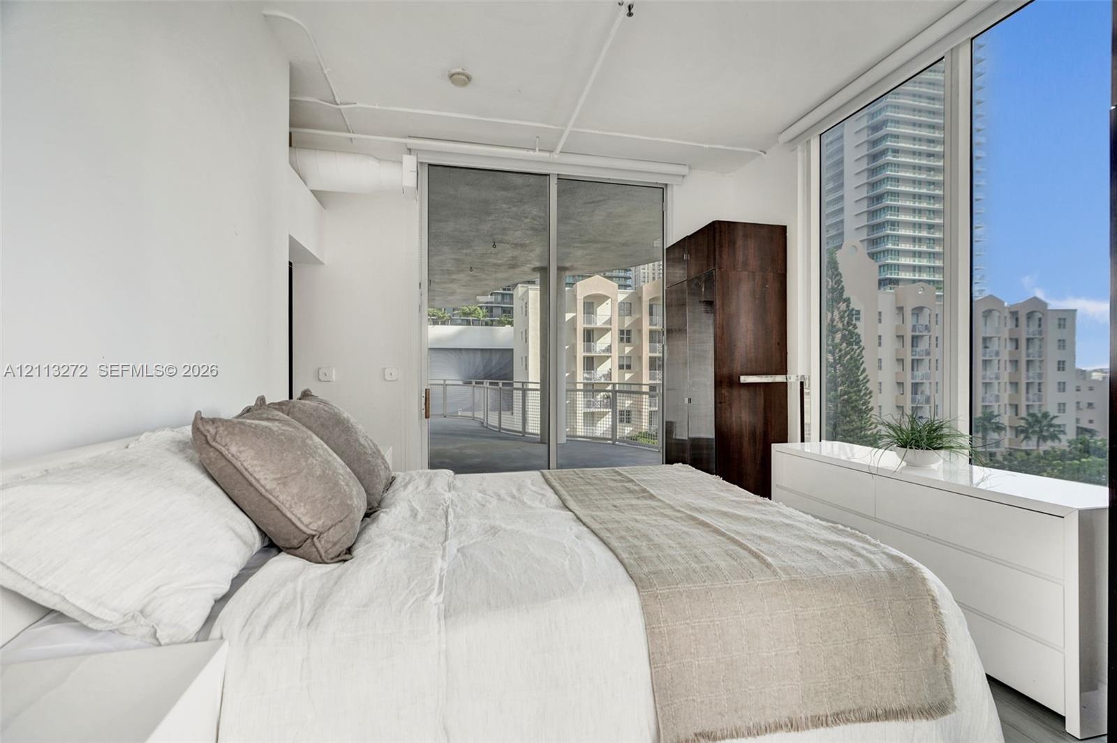 Floor-to-ceiling windows, sliding glass door access to an exterior balcony, industrial-style exposed ceiling, and built-in dark wood cabinetry