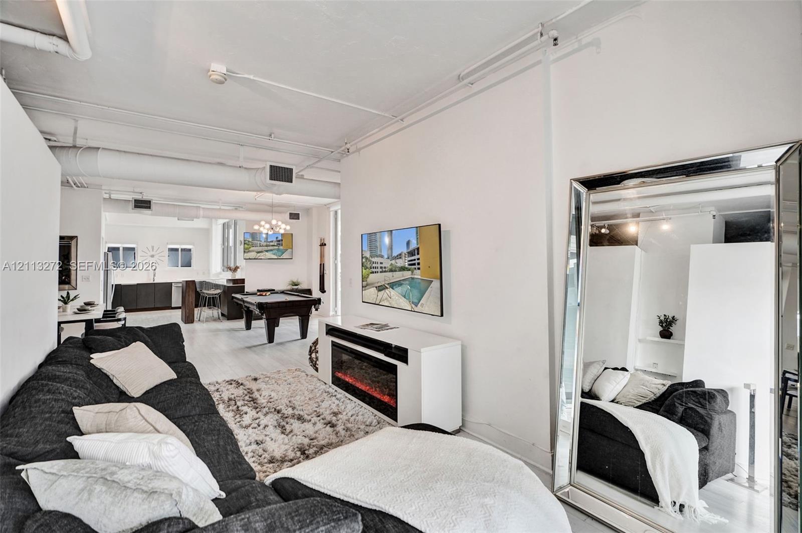 Open-concept floor plan featuring high ceilings with exposed industrial-style ductwork, white-painted masonry walls, and neutral flooring