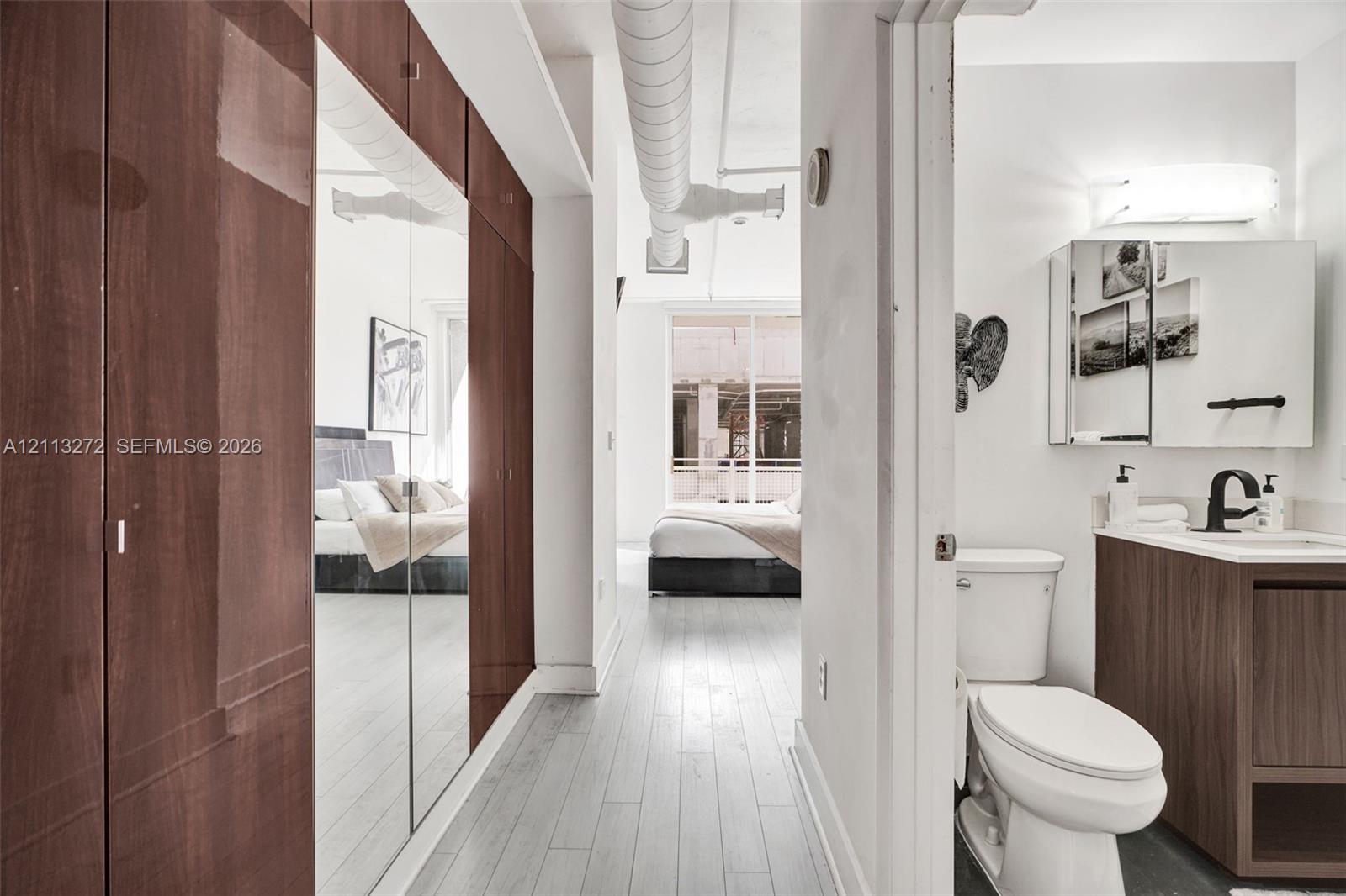 Floor-to-ceiling cabinetry with mirrored doors, wood-finish flooring, industrial exposed ductwork, and vanity with an integrated sink and matte black faucet