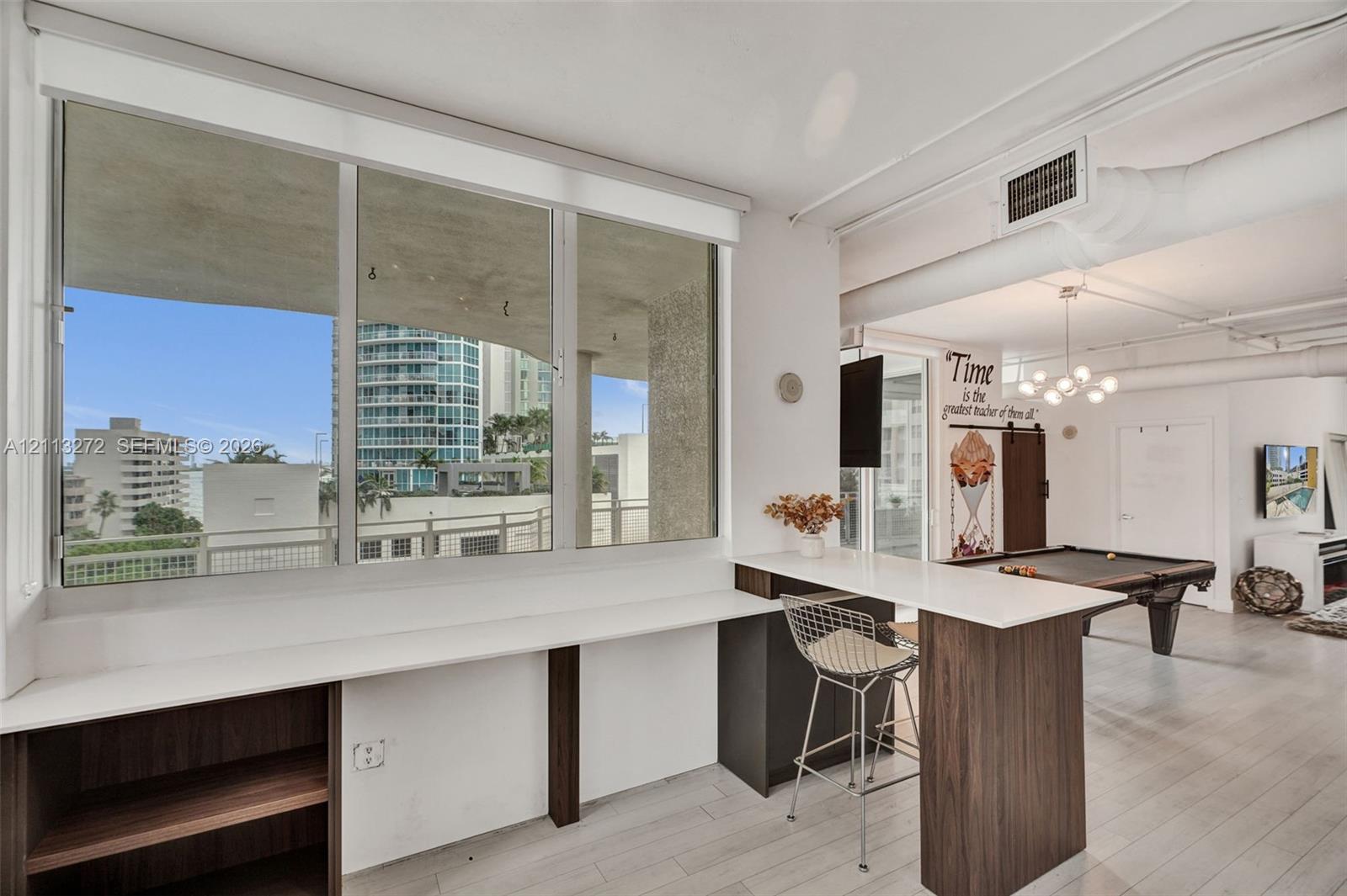Built-in desk with quartz countertop and wood-finish cabinetry, floor-to-ceiling windows, light-toned tile flooring, exposed ceiling ductwork, and multi-light hanging fixture