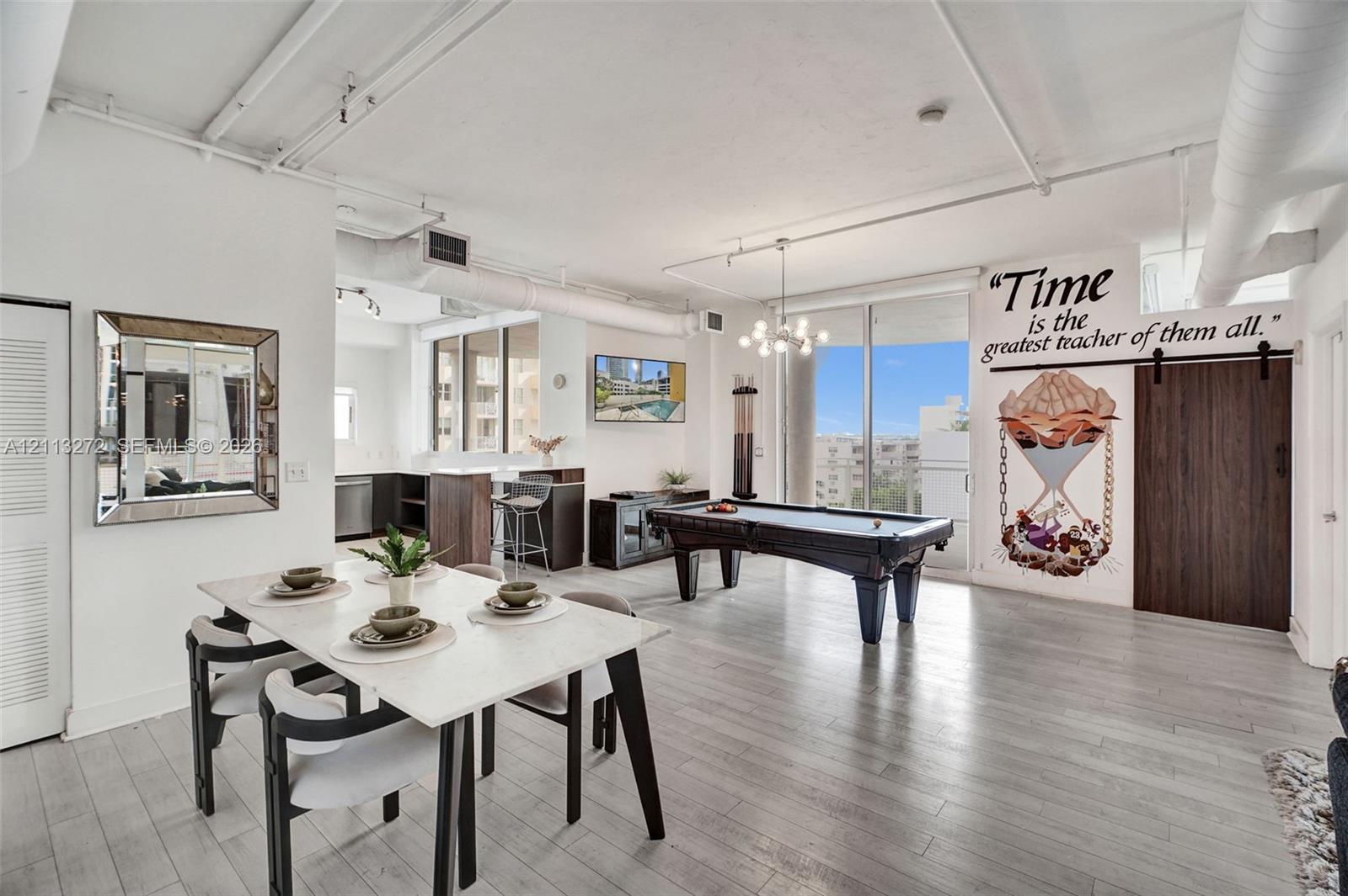 Open-concept interior featuring light wood-finish flooring, exposed industrial-style ceiling ductwork, floor-to-ceiling windows, and a dark wood barn-style sliding door