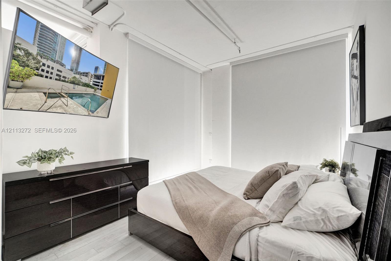 High-ceiling room featuring white walls, light-toned flooring, and wall-to-wall automated roller shades