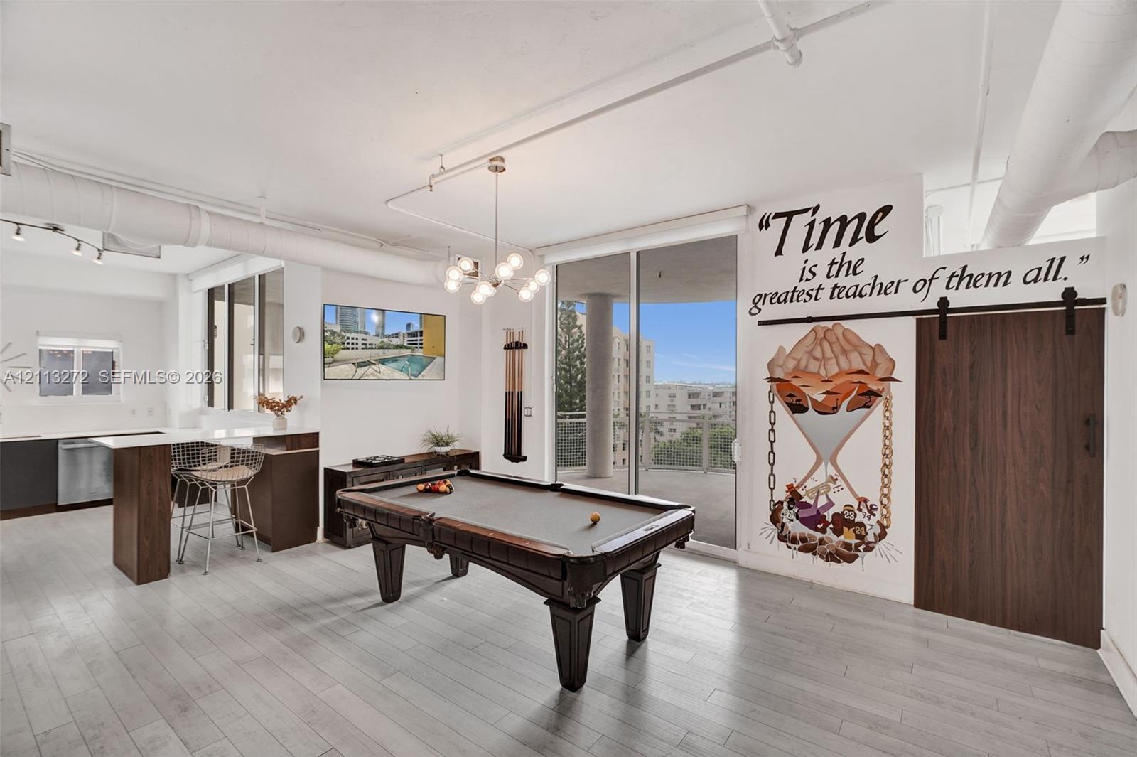 Open-concept living space featuring wood-finish flooring, exposed overhead industrial piping, a multi-globe chandelier, and a wood-panel sliding barn door with matte black hardware