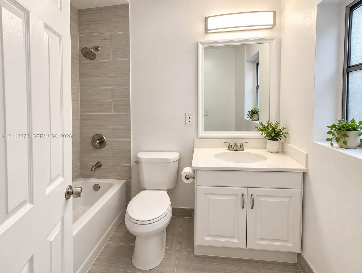 Bathroom featuring a white vanity with a solid-surface countertop, an integrated sink, polished chrome fixtures, a tiled tub surround, and ceramic floor tiling Bathroom featuring a white vanity with a solid-surface countertop, an integrated sink, polished chrome fixtures, a tiled tub surround, and ceramic floor tiling