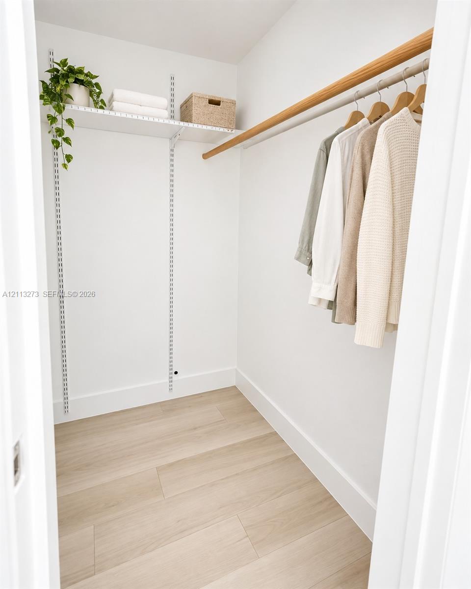 Storage space featuring adjustable metal shelving, a wall-mounted wood closet rod, and light-toned wood-finish flooring Storage space featuring adjustable metal shelving, a wall-mounted wood closet rod, and light-toned wood-finish flooring
